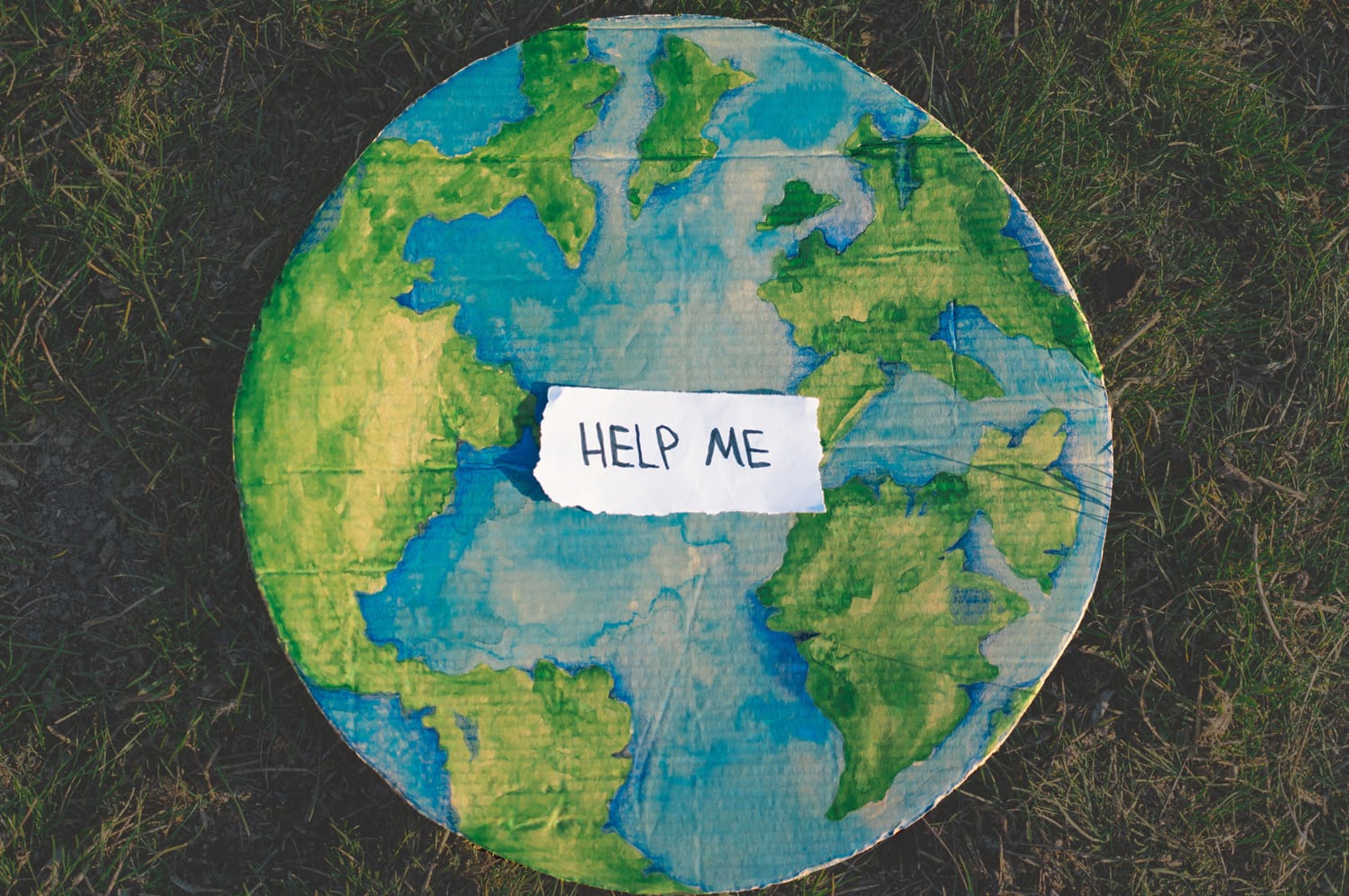 Gemalte Erde mit einem Zettel darauf, auf dem "Help me" steht